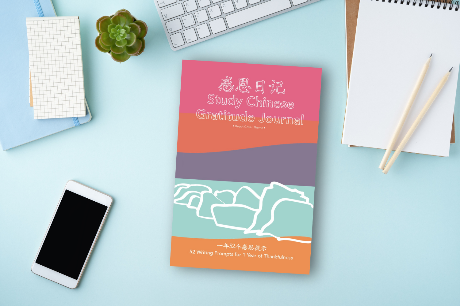 Copy of the book Study Chinese Gratitude Journal 感恩日记: 一年52个感恩提示 / 52 Writing Prompts for 1 Year of Thankfulness (Beach Cover Theme) sitting on a light blue desktop next to a phone and office supplies